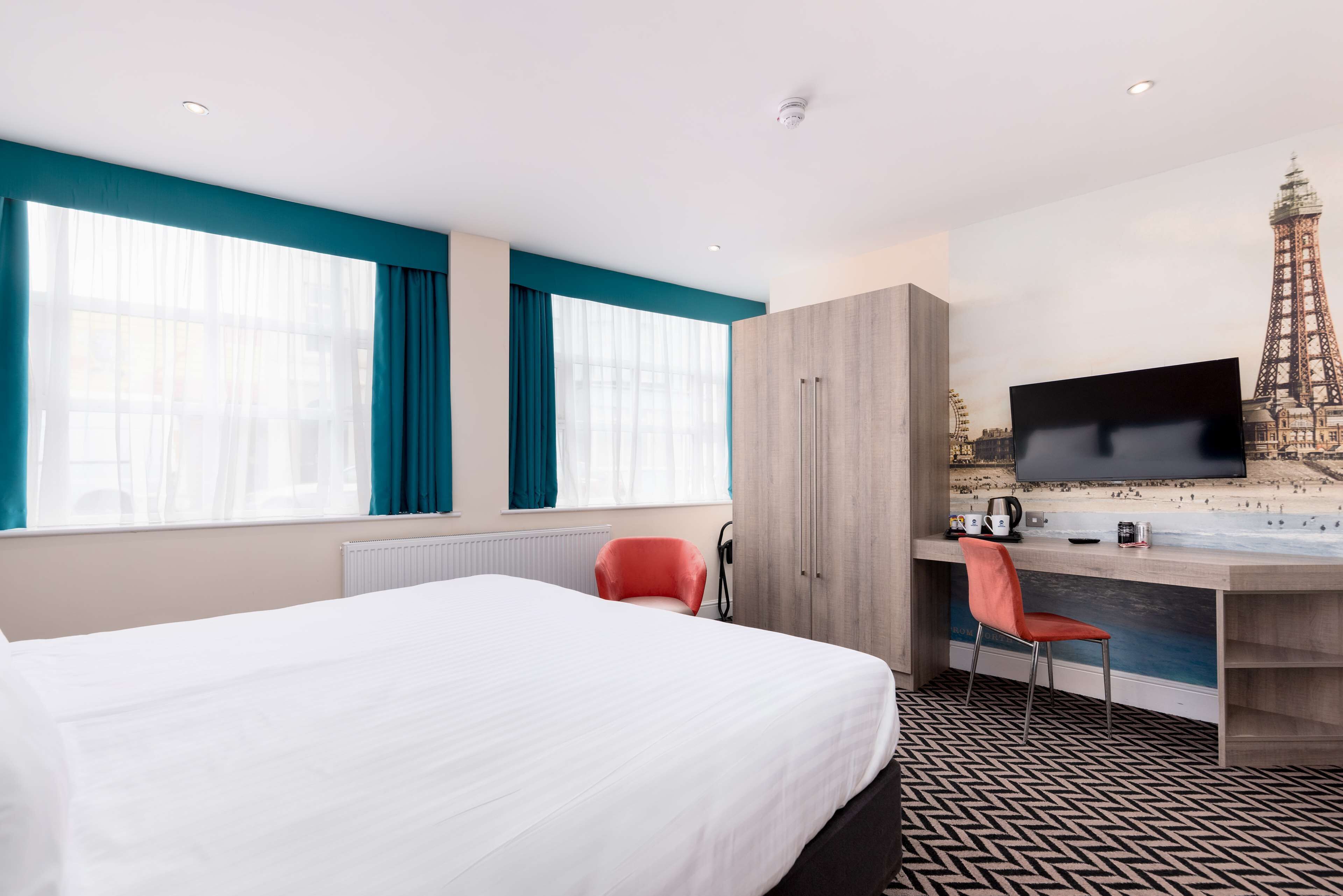 A hotel room with a bed, a desk with a chair, a television, and a view of the Eiffel Tower.