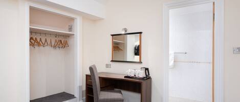 A hotel room with a desk, chair, and a walk-in closet with wooden hangers.