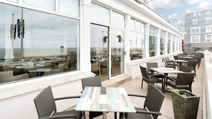 An outdoor seating area with tables and chairs, large windows, and a view of the sea. - Best Western Carlton Hotel (Blackpool)