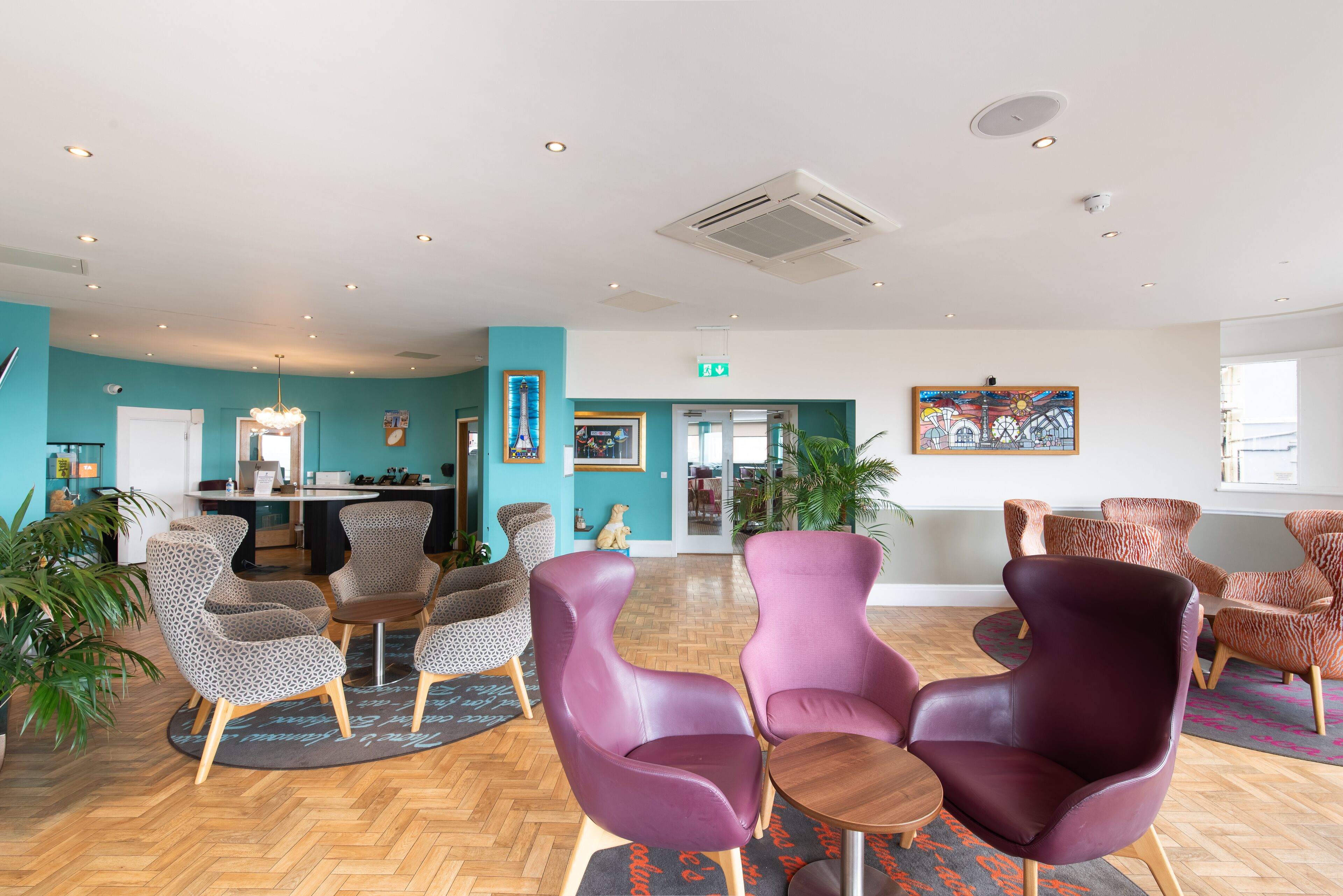 A spacious lobby with patterned chairs, a reception desk, and a large painting on the wall.