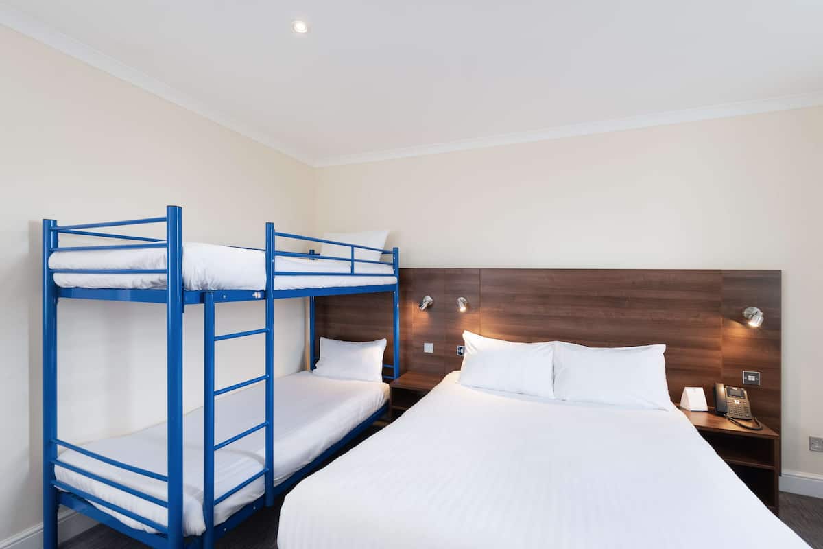A hotel room with bunk beds, a large bed, a wooden headboard, bedside lamps, and a telephone.