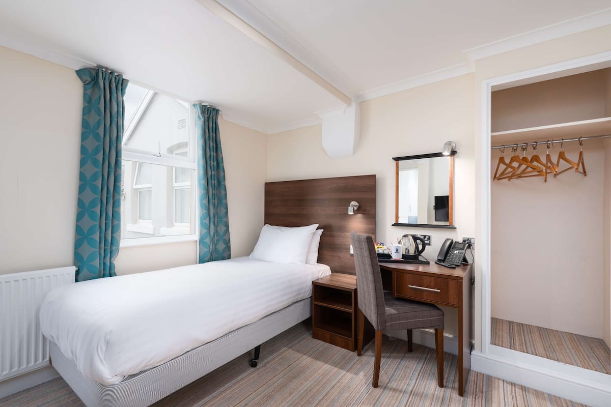 A hotel room with a bed, a desk with a chair, a telephone, and a mirror.