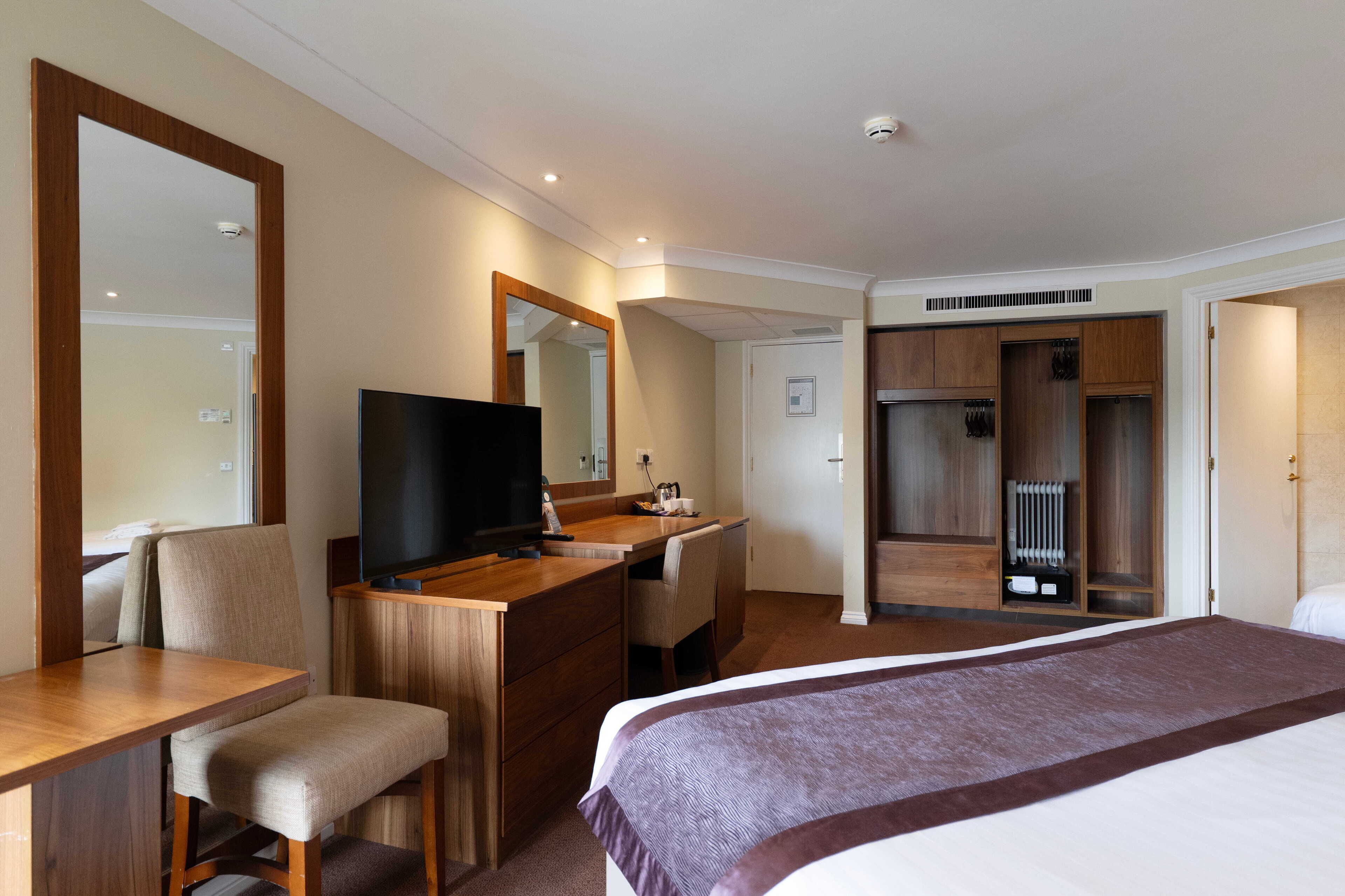 Une chambre d’hôtel comprenant un lit, un bureau avec une télévision, un miroir, une armoire et une salle de bain.