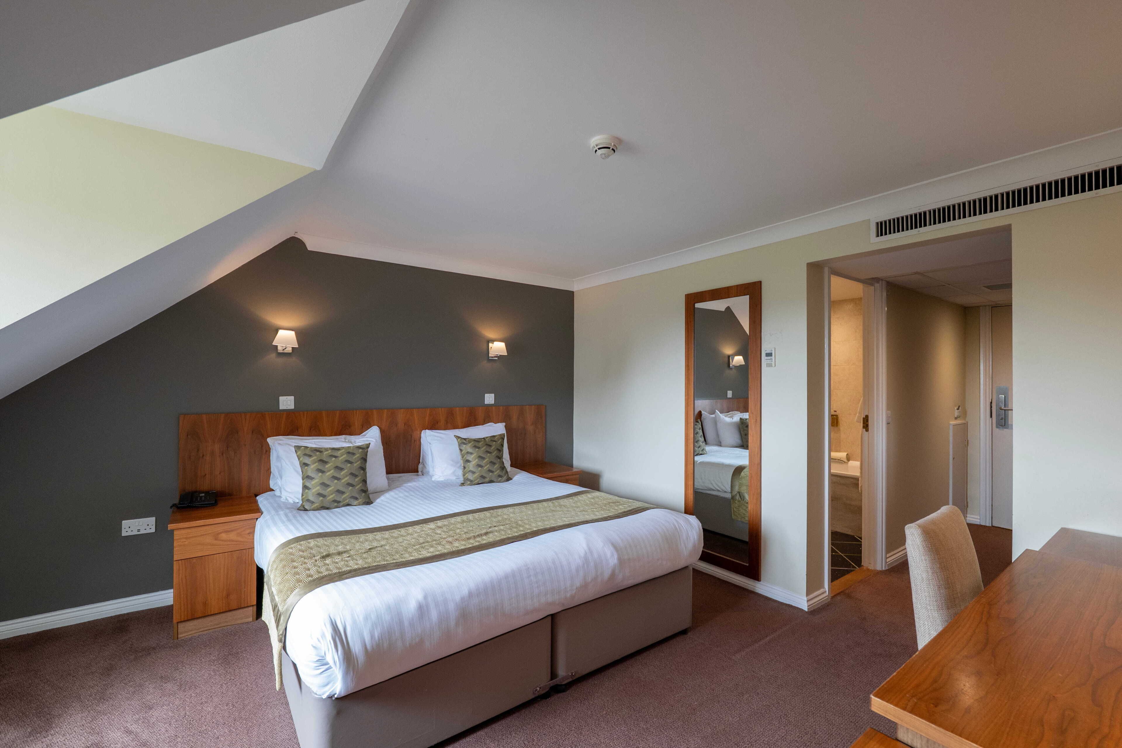 A bedroom with a large bed, bedside lamps, a wooden headboard, and a mirror.
