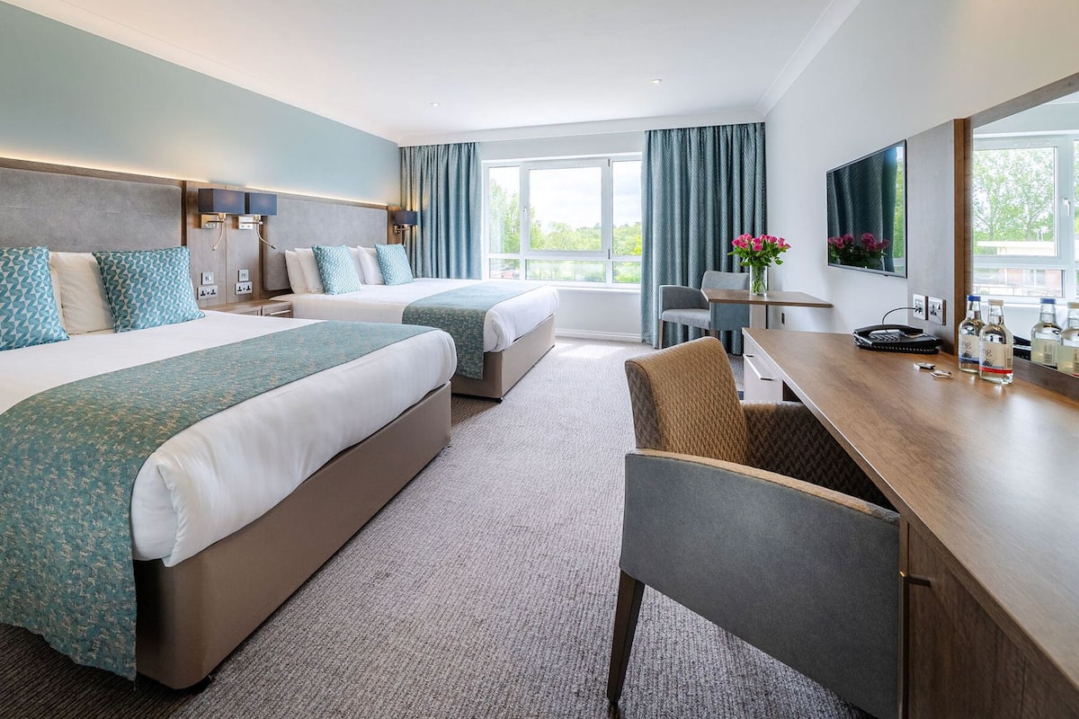 A hotel room with two beds, a desk, and a chair.