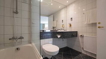 A modern bathroom with a glass-enclosed shower, a white toilet, a marble-tiled floor, and a vanity with a mirror and toiletries.