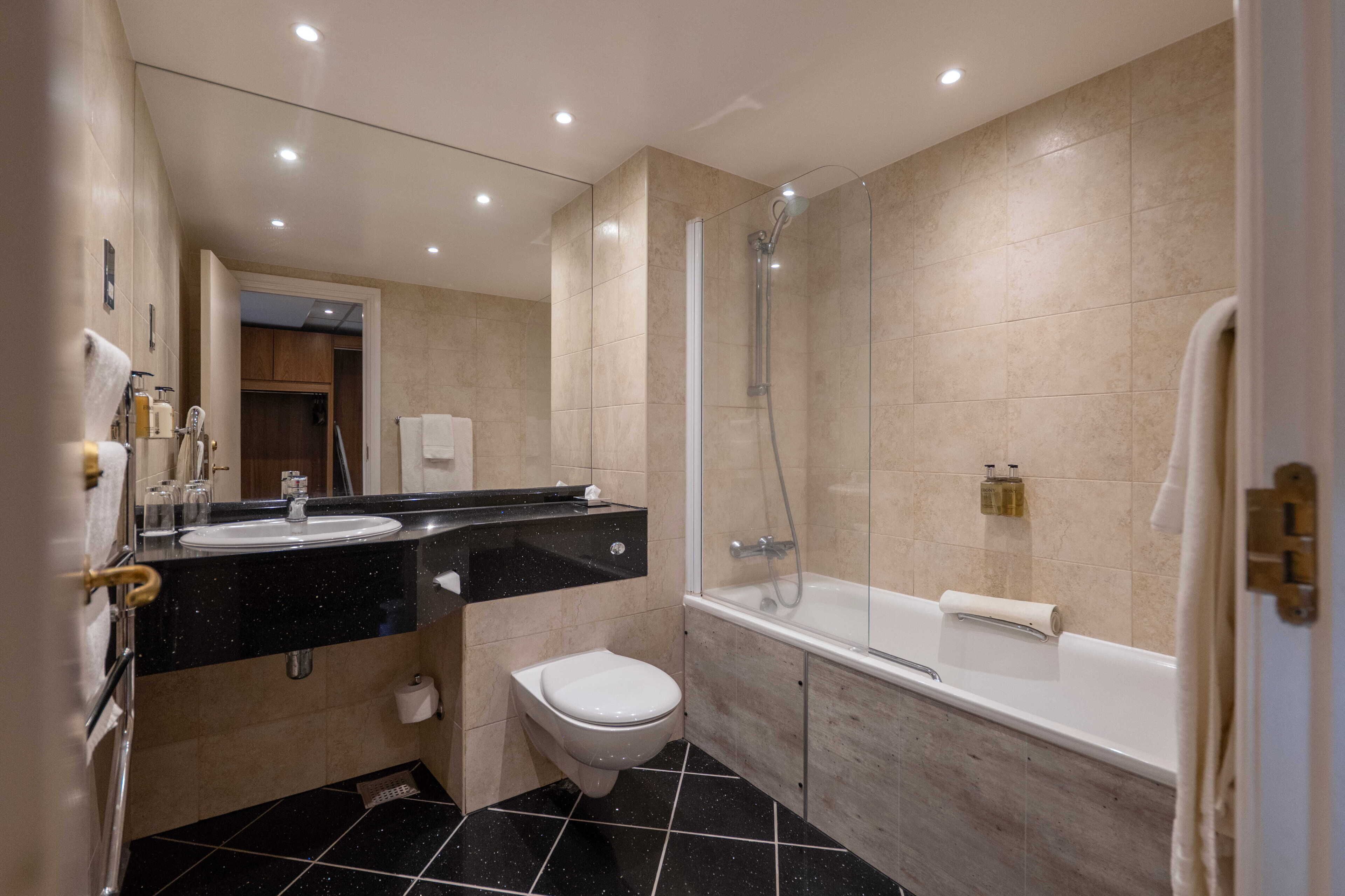 A modern bathroom with a black countertop sink, a white toilet, a glass-enclosed shower, and a bathtub.