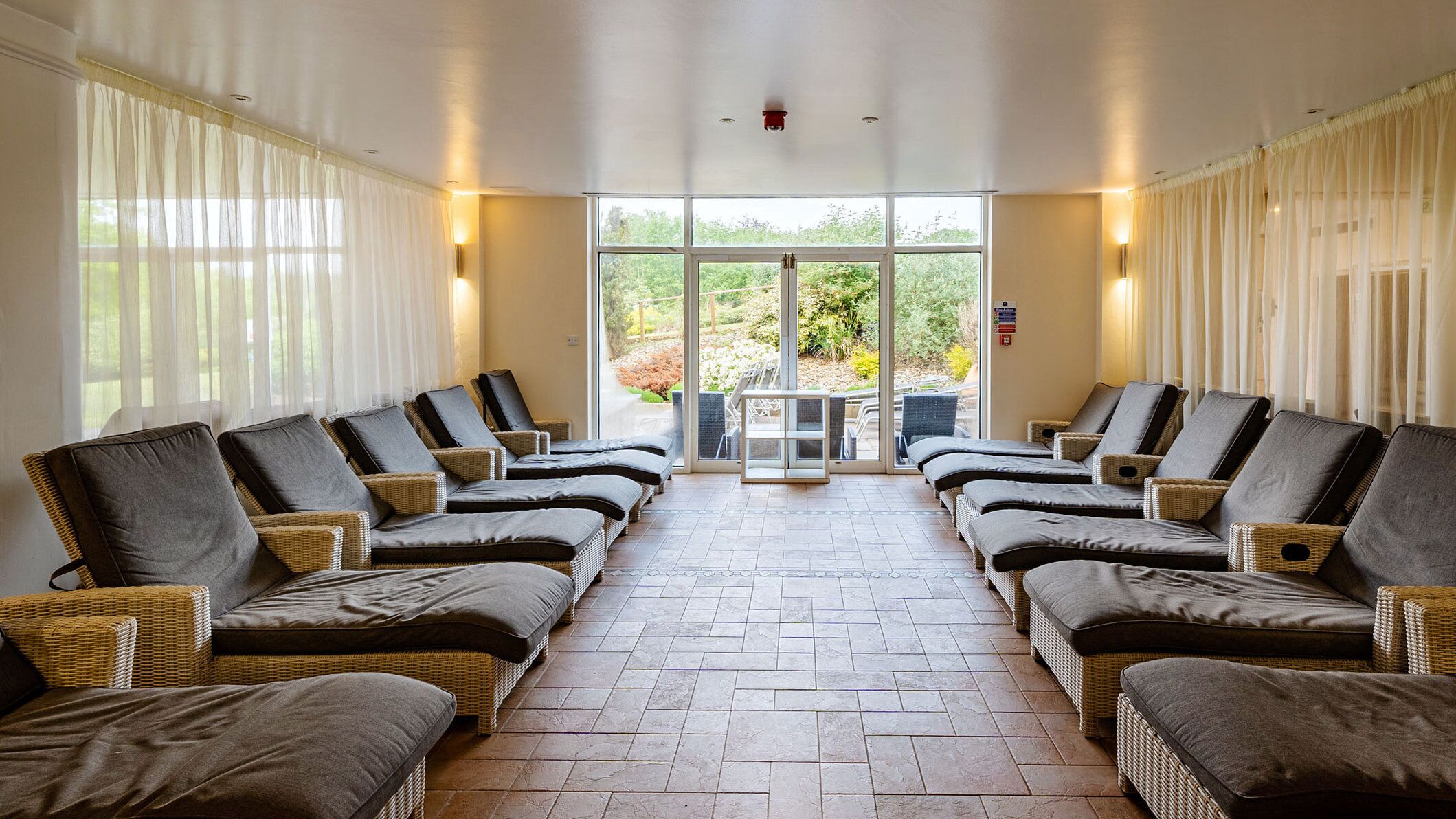 A spa room with multiple reclining chairs, a tiled floor, and large windows with curtains.