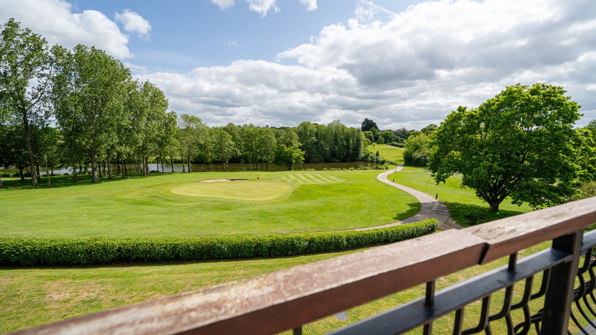 A golf course with a wooden fence, a pond, and trees.