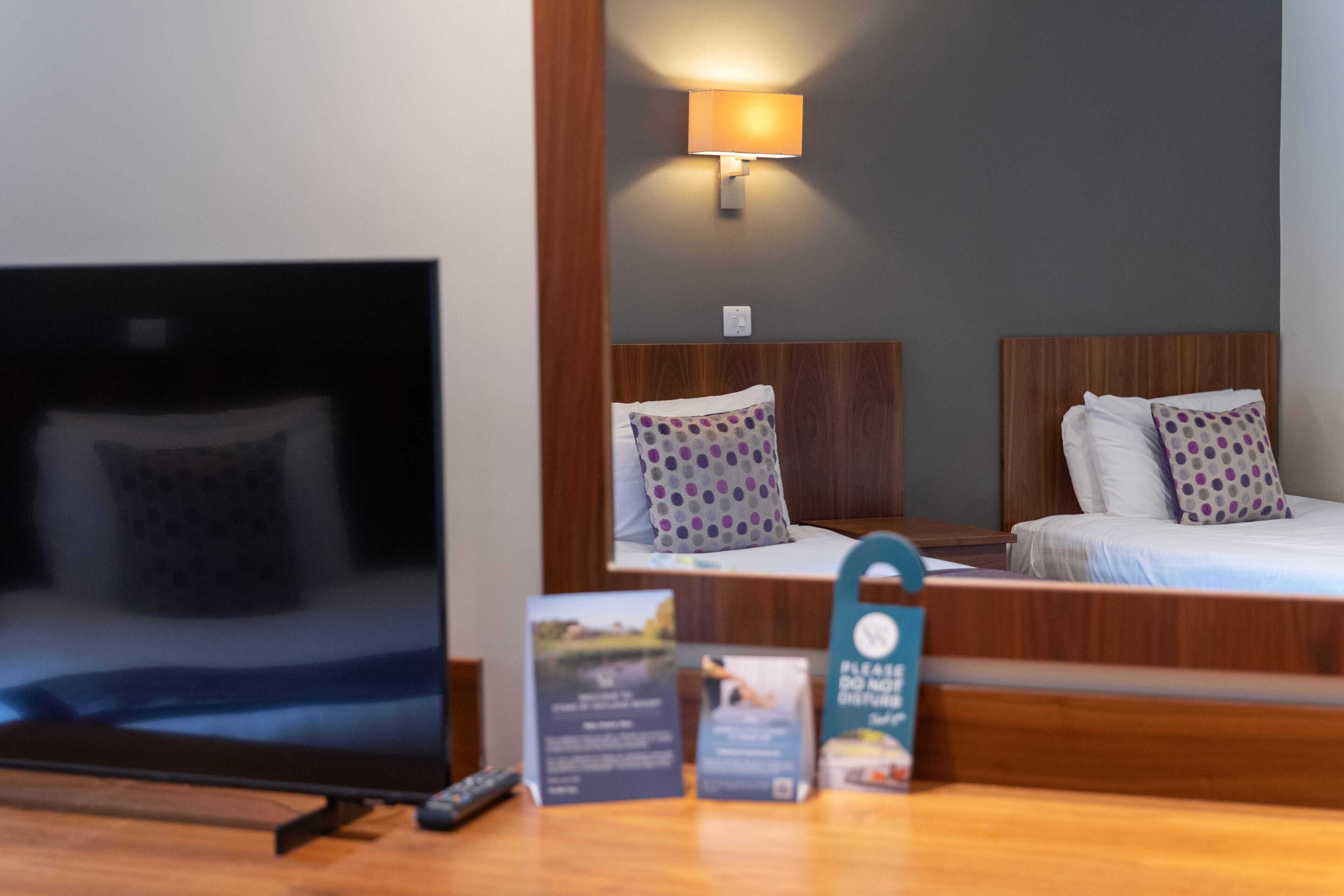 A hotel room with a bed, a TV, and a bedside table with a remote control.