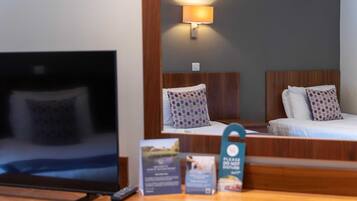 A hotel room with a bed, a TV, and a bedside table with a remote control.