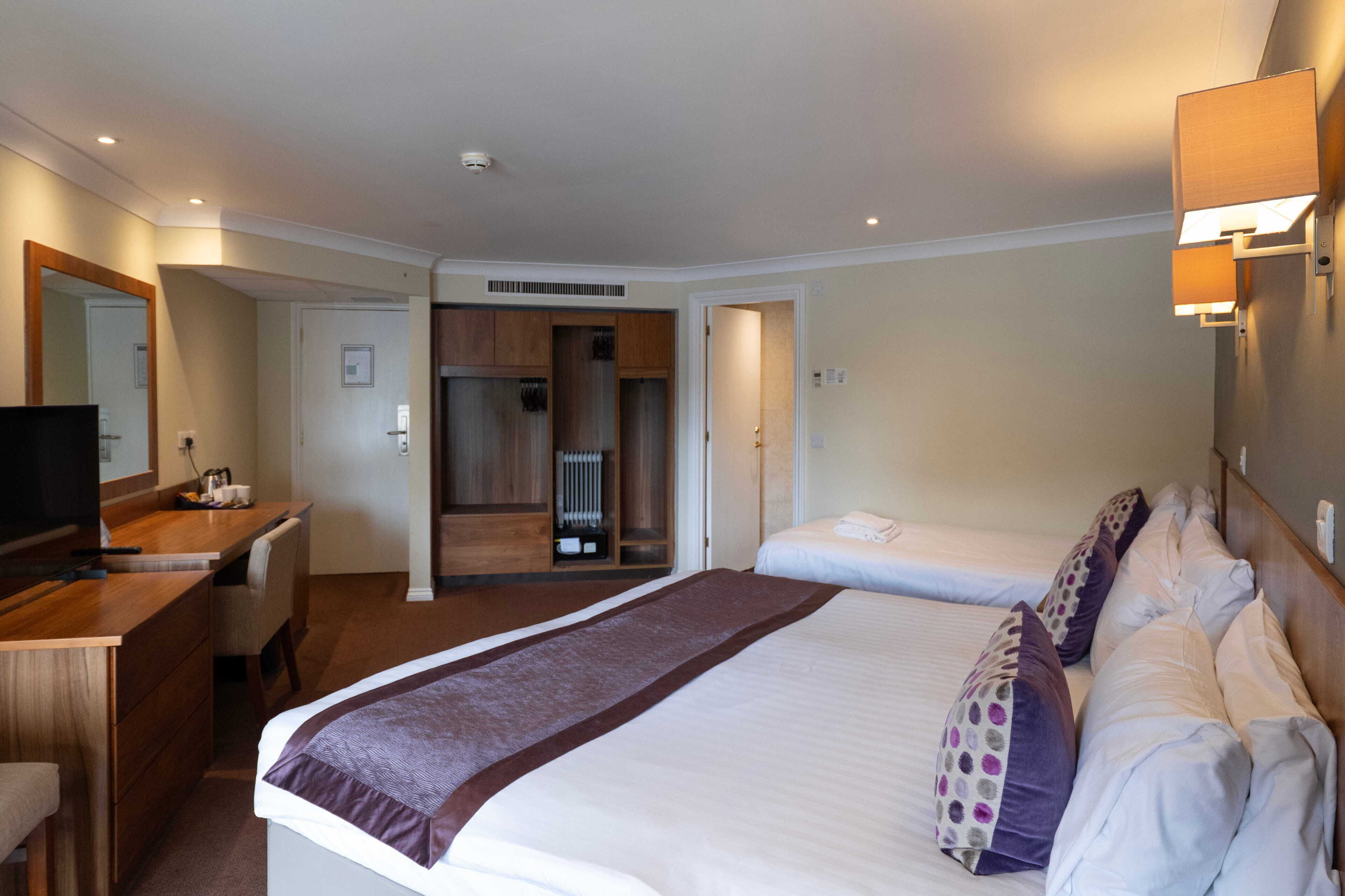 A hotel room with a large bed, a desk, a television, and a bathroom visible through an open door.