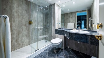 Un baño moderno con cabina de ducha de vidrio, inodoro blanco, lavabo con encimera de granito y un espejo grande.