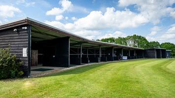 A stable with covered stalls and a grassy area in front.