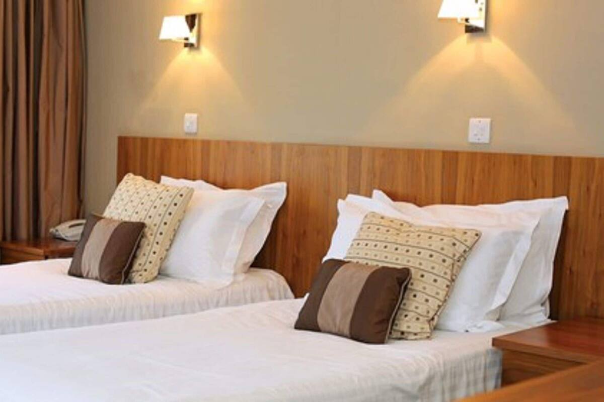 A hotel room with two beds, wooden headboards, and wall-mounted lights.