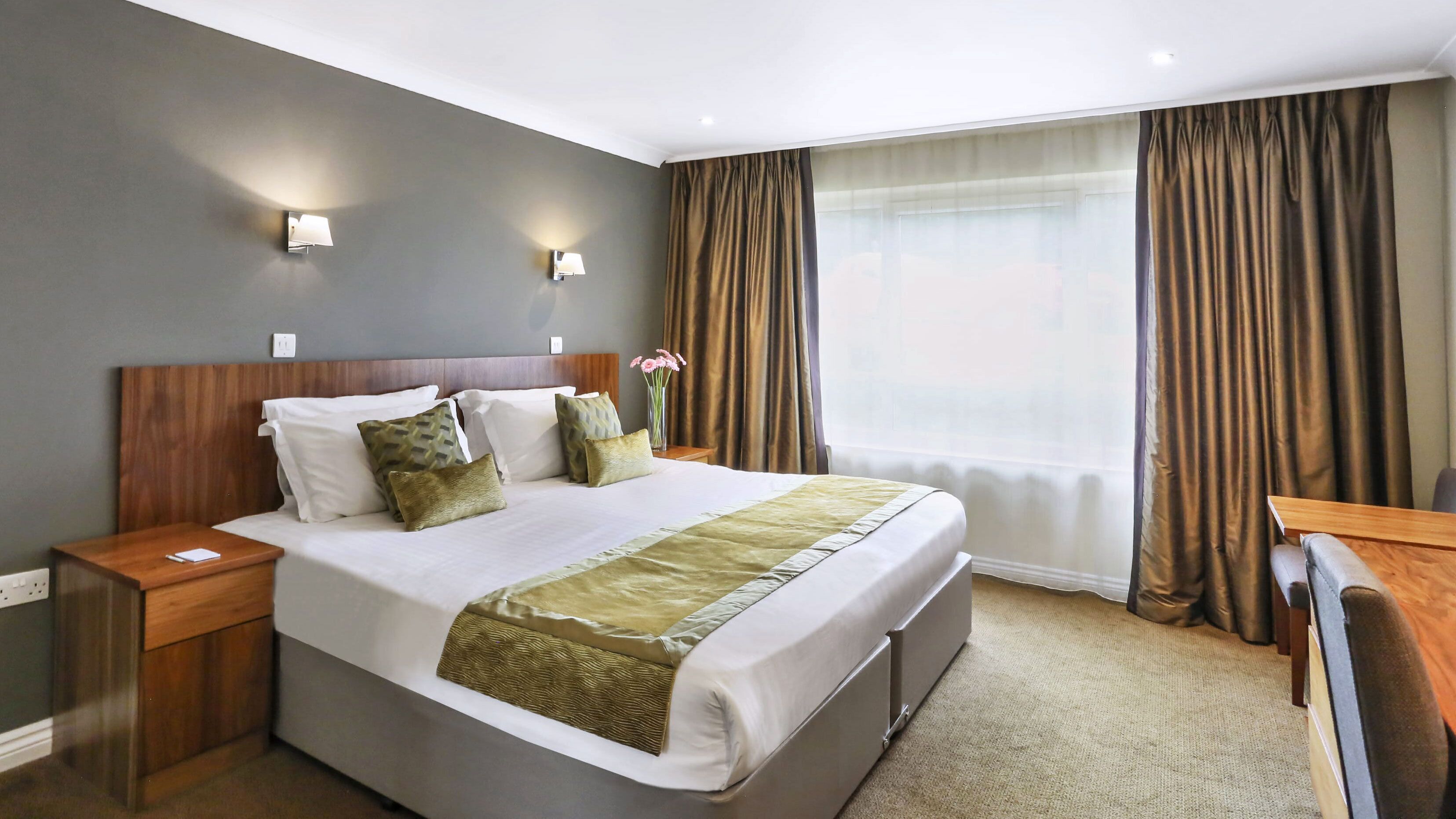 A hotel room with a large bed, two bedside tables, a nightstand, a desk, and a window with curtains.