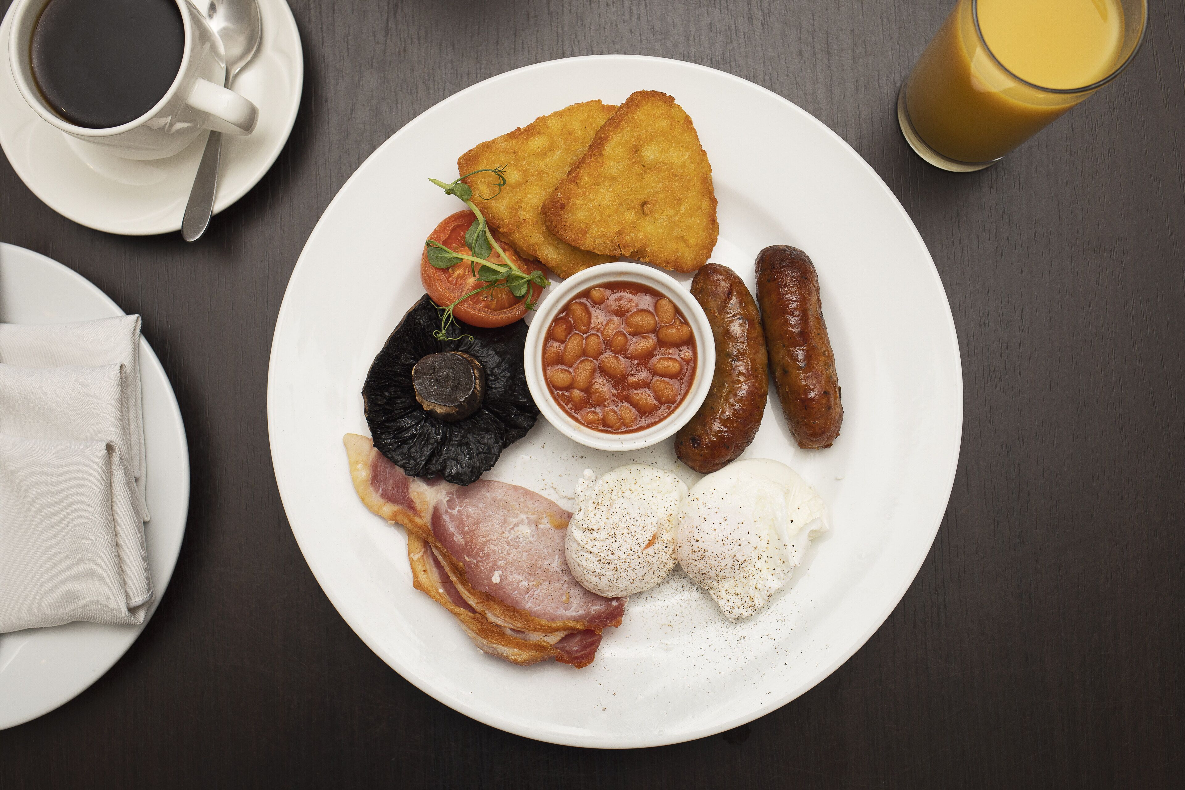 A breakfast plate with eggs, sausages, bacon, baked beans, and toast.