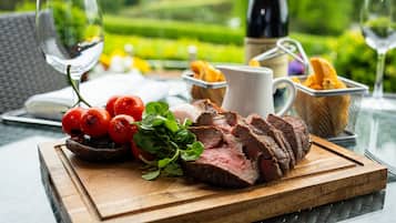 A wooden cutting board with sliced beef, cherry tomatoes, and greens on an outdoor table.