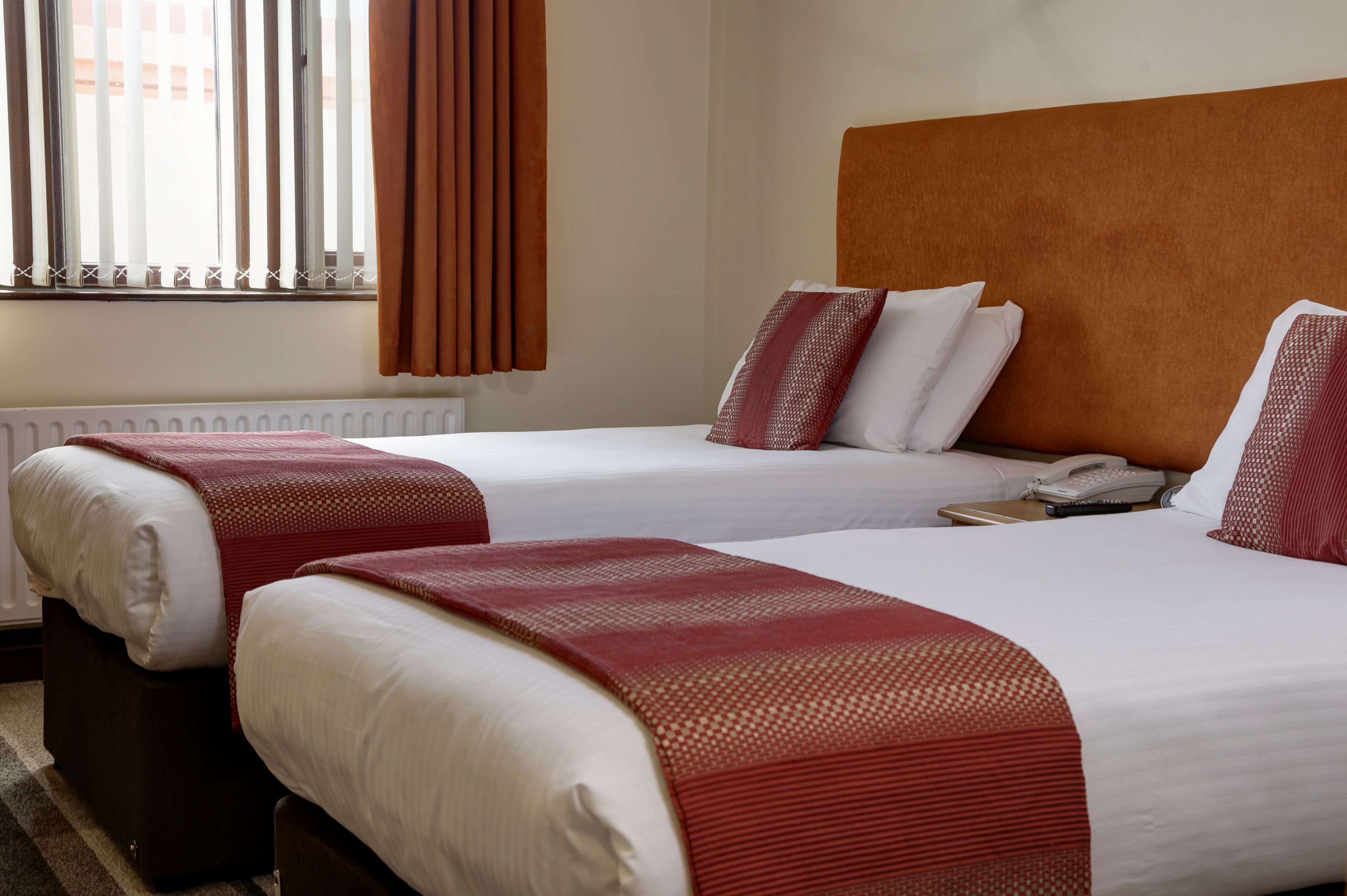 Een hotelkamer met twee bedden, een houten hoofdeinde, een telefoon en een raam met gordijnen.