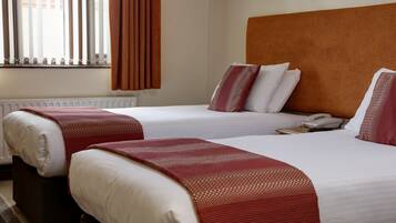 Een hotelkamer met twee bedden, een houten hoofdeinde, een telefoon en een raam met gordijnen.