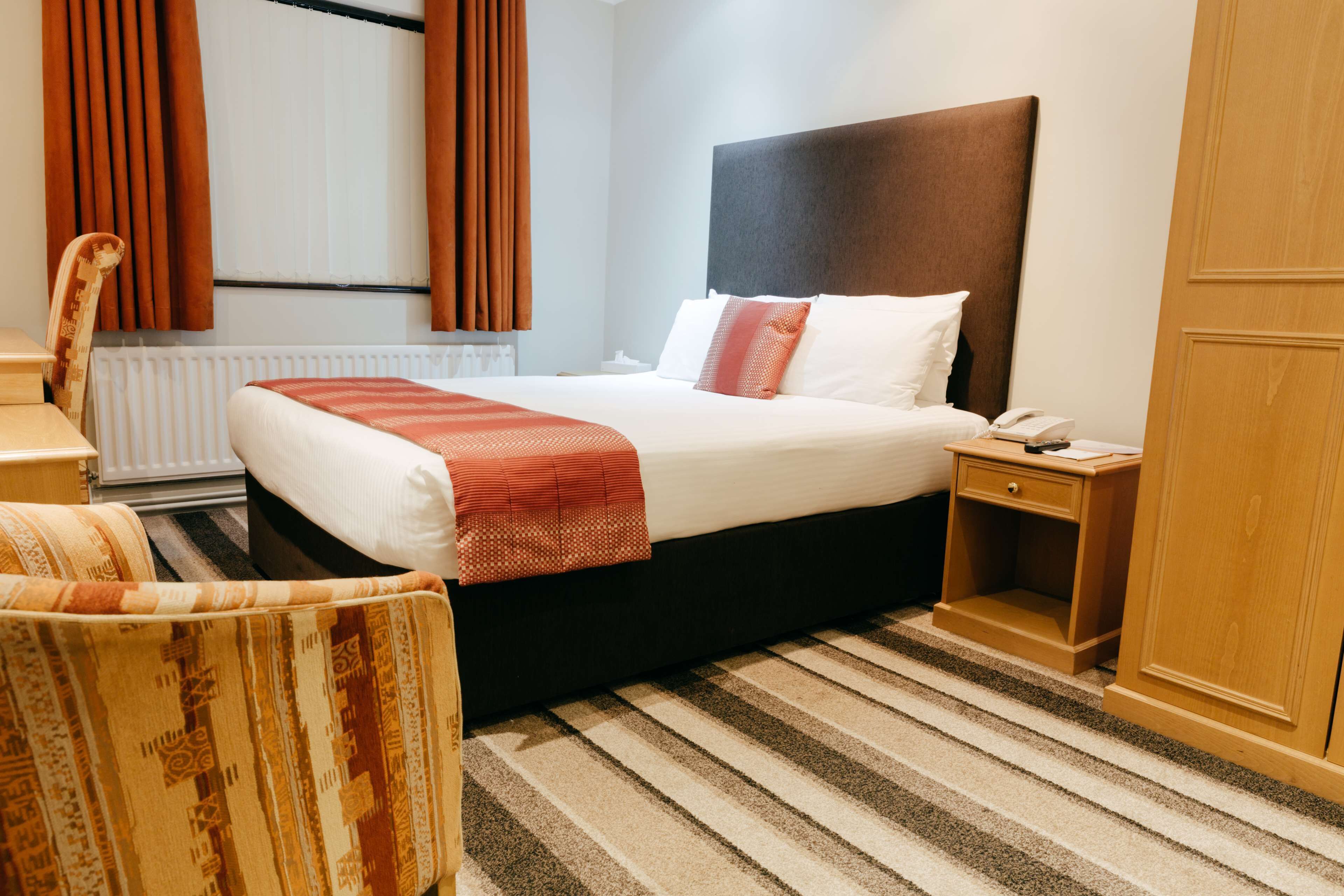 Una habitación de hotel con una cama grande, una mesita de noche, una silla y un armario de madera.