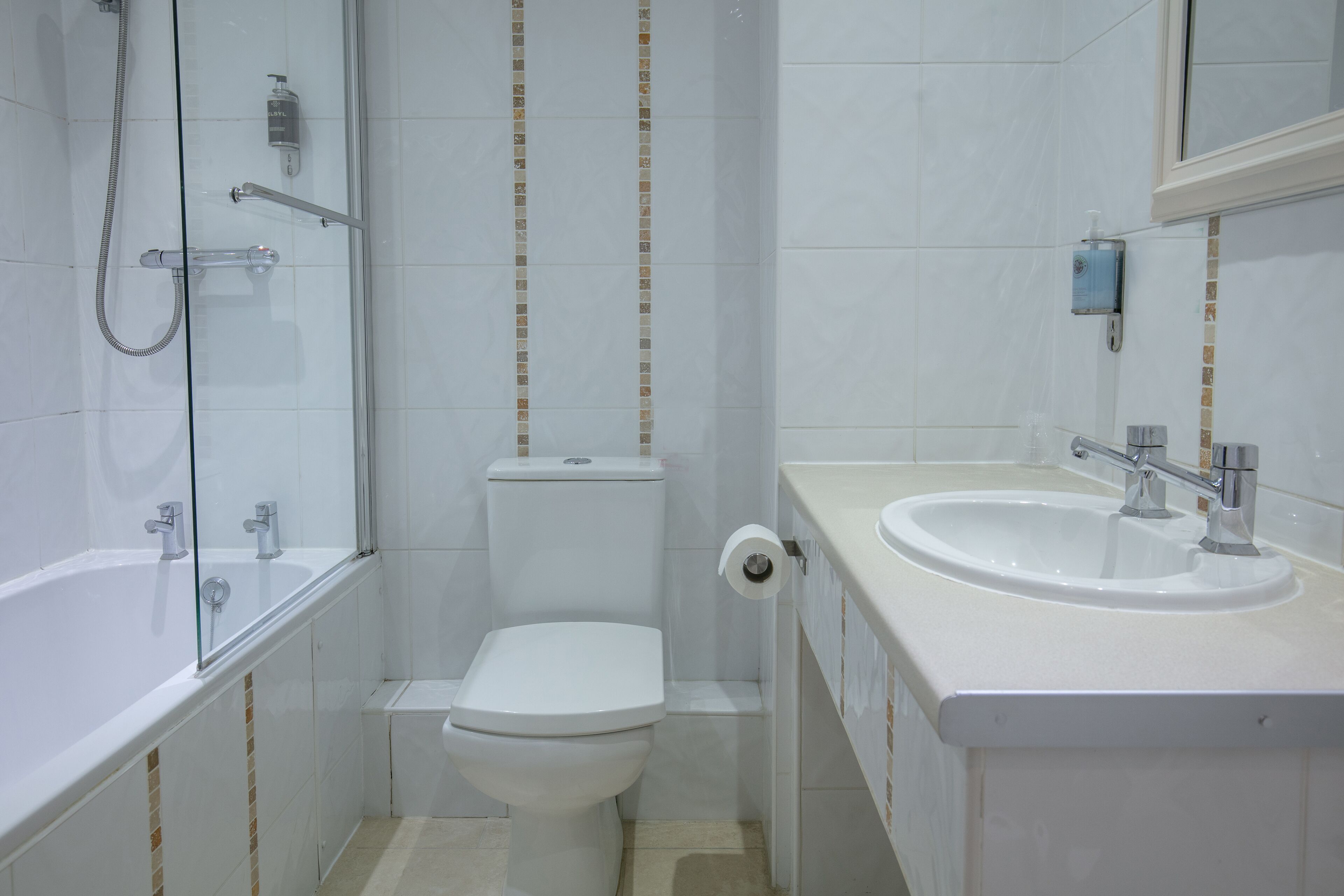 Un baño moderno con ducha envuelta en vidrio, inodoro y lavamanos con espejo superior.