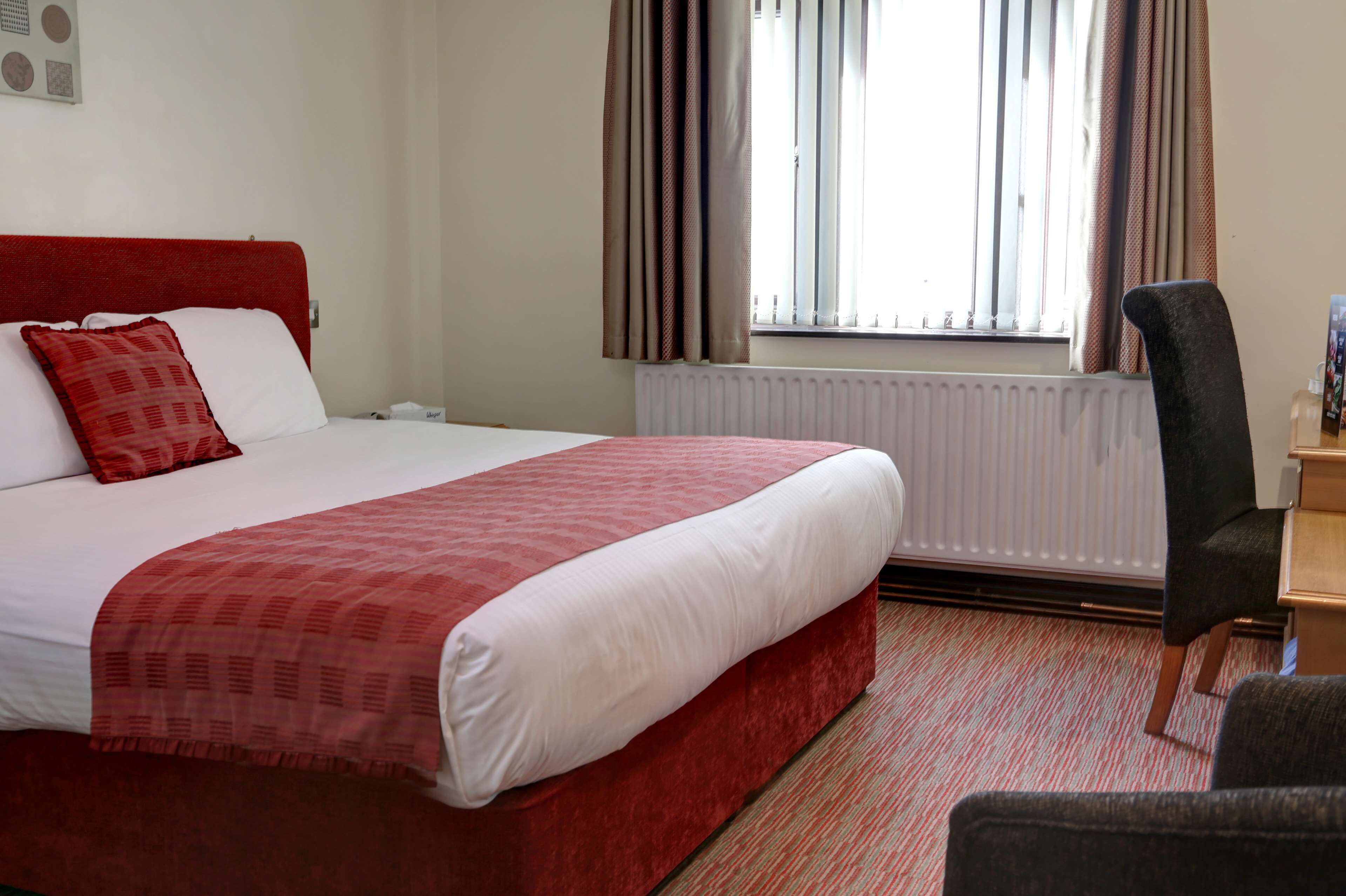 Una habitación de hotel con cama, una silla, un radiador y una ventana con cortinas.