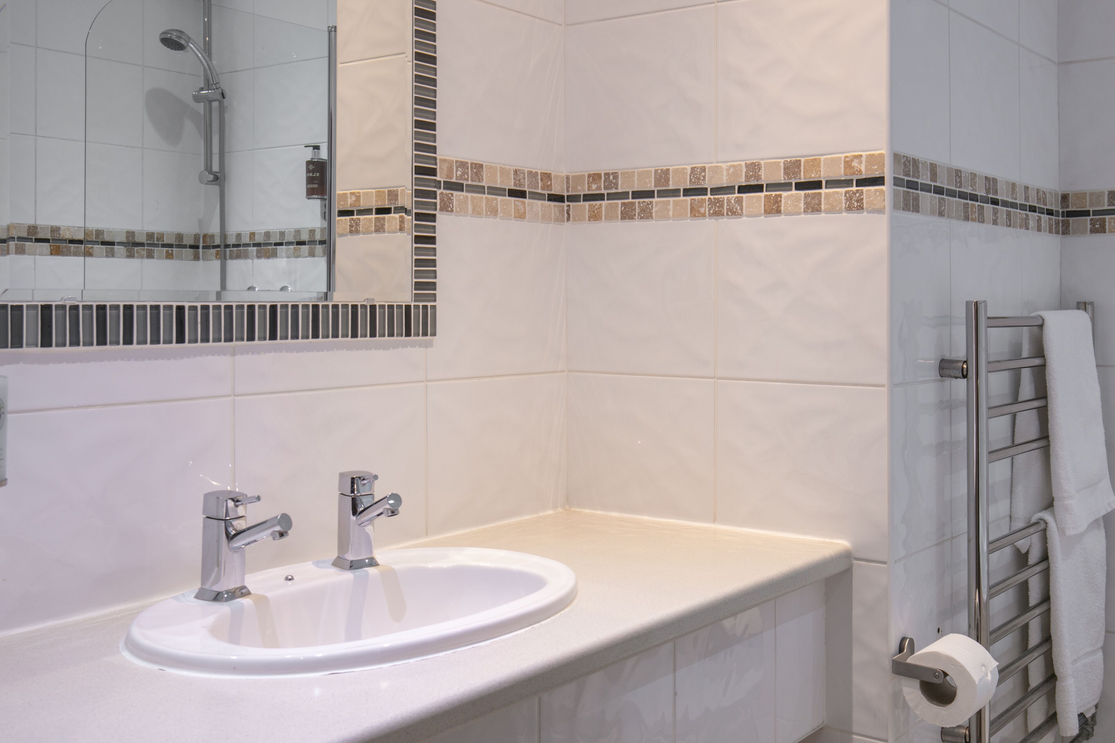 A bathroom with a white sink, two faucets, a showerhead, and a towel rack.