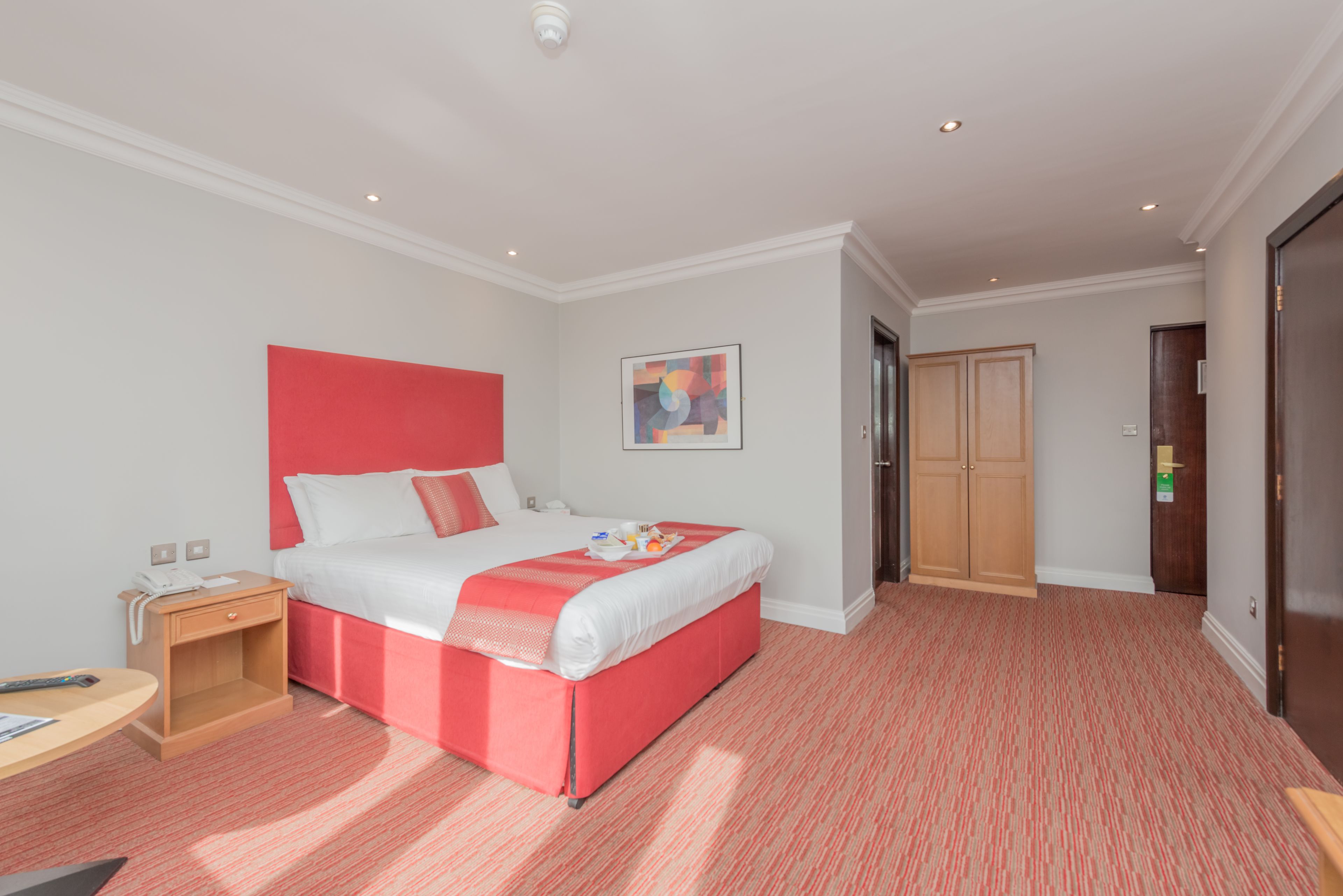 A hotel room with a large bed, a bedside table, a desk, and a door.