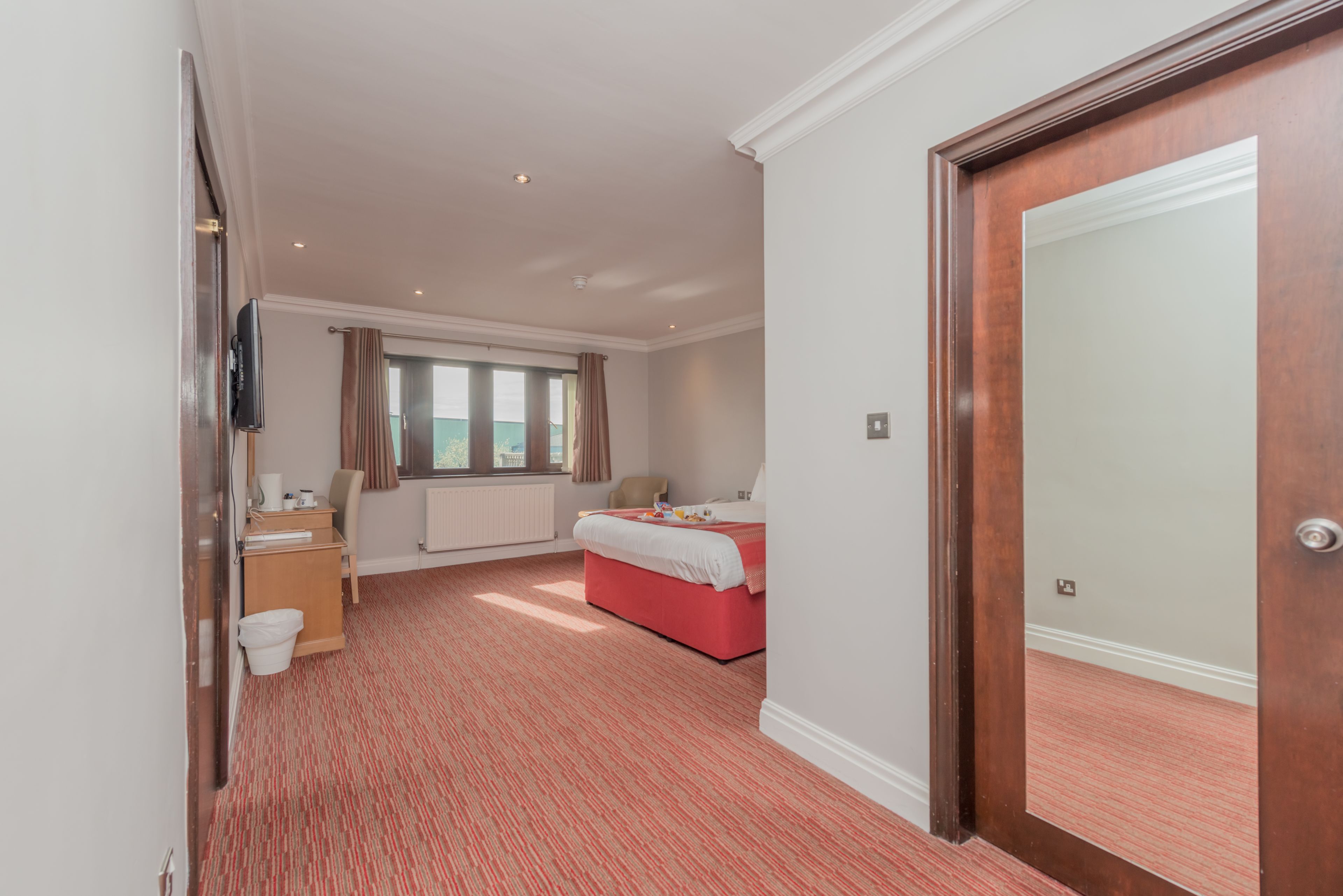 Ein Hotelzimmer mit Bett, Fenster, Heizkörper, Fernseher und Tür.