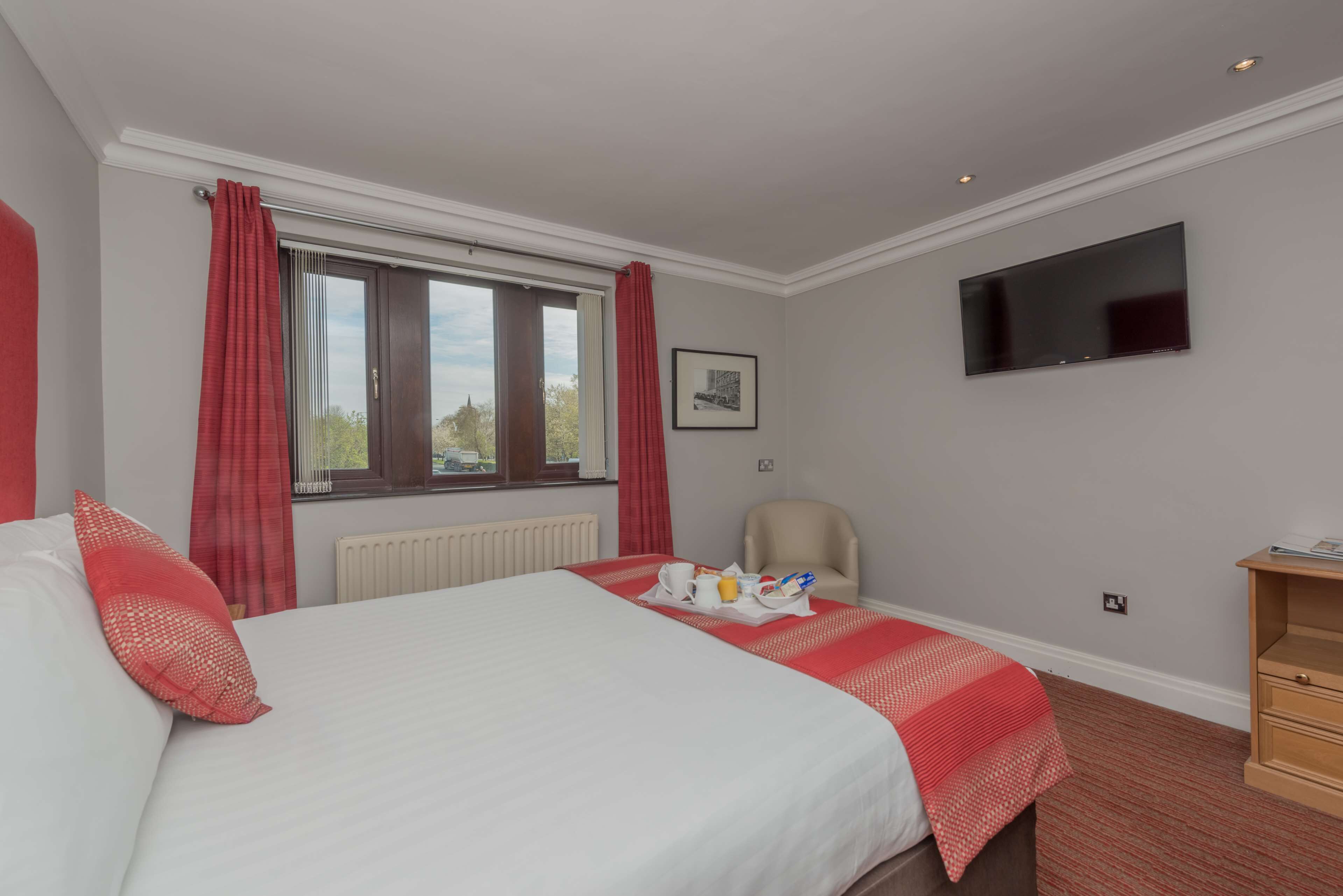 Une chambre d’hôtel avec un lit, une chaise, une télévision et une fenêtre avec des rideaux.