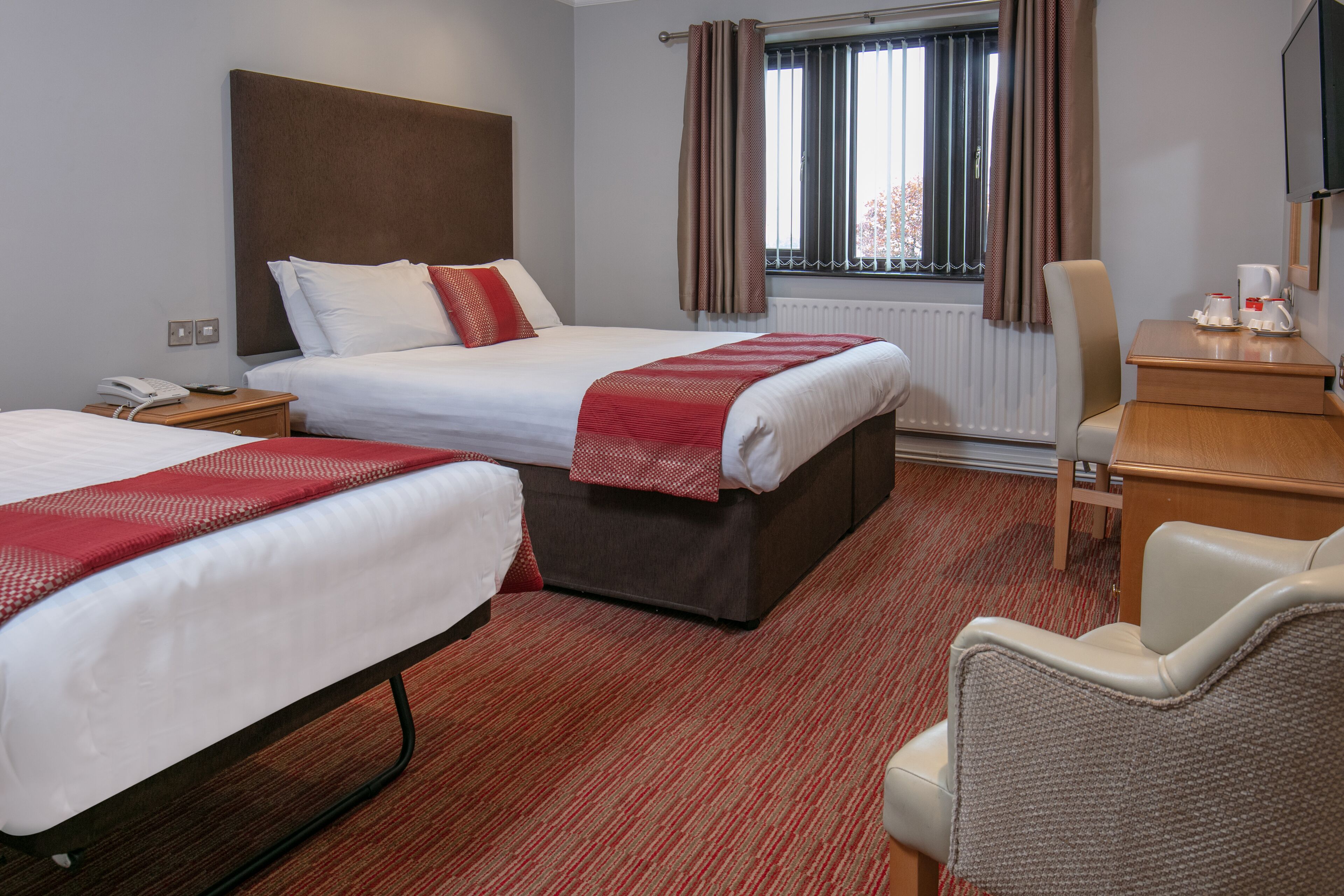 A hotel room with two beds, a desk, a chair, a telephone, and a window with curtains.