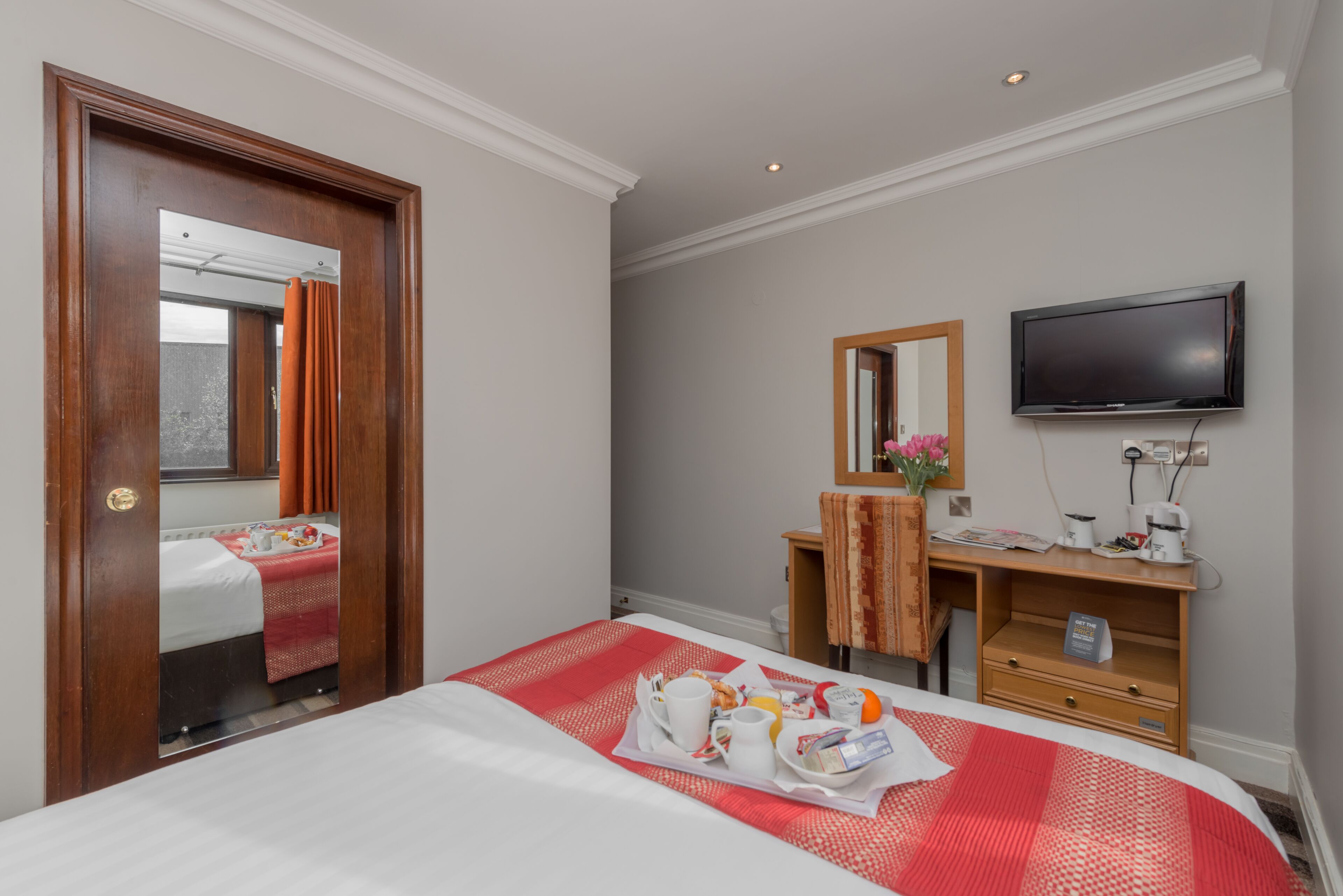 A hotel room with a bed, a desk with a flat-screen TV, and a breakfast tray on the bed.