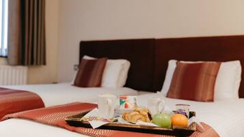 A hotel room with a neatly made bed, a tray with breakfast items, and a window with curtains.