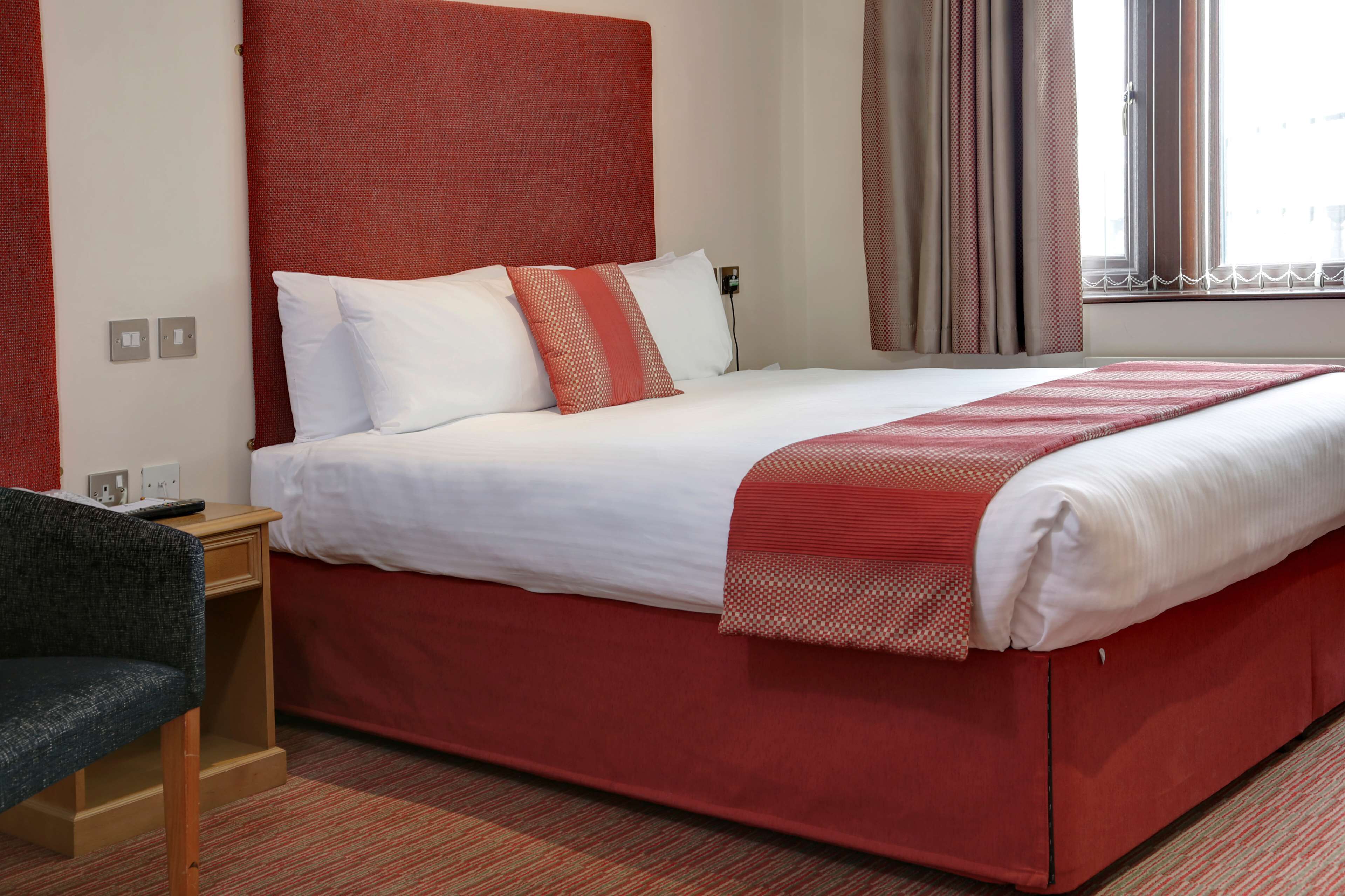 Une chambre d’hôtel avec un grand lit, une table de chevet en bois, une chaise et une fenêtre avec des rideaux.