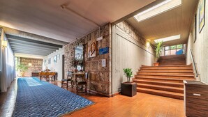 A spacious lobby with a wooden staircase, a blue patterned rug, and a stone wall with a clock. - Garden Hotel (Terni)