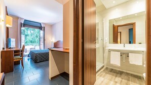 A hotel room with a desk, chair, bed, and a bathroom with a sink and mirror. - Garden Hotel (Terni)