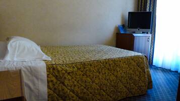 A hotel room with a bed, a television on a cabinet, and a window with curtains.