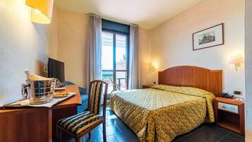 Ein Hotelzimmer mit einem Bett, einem Schreibtisch mit Computer, einem Sessel und einem Fenster mit Vorhängen.