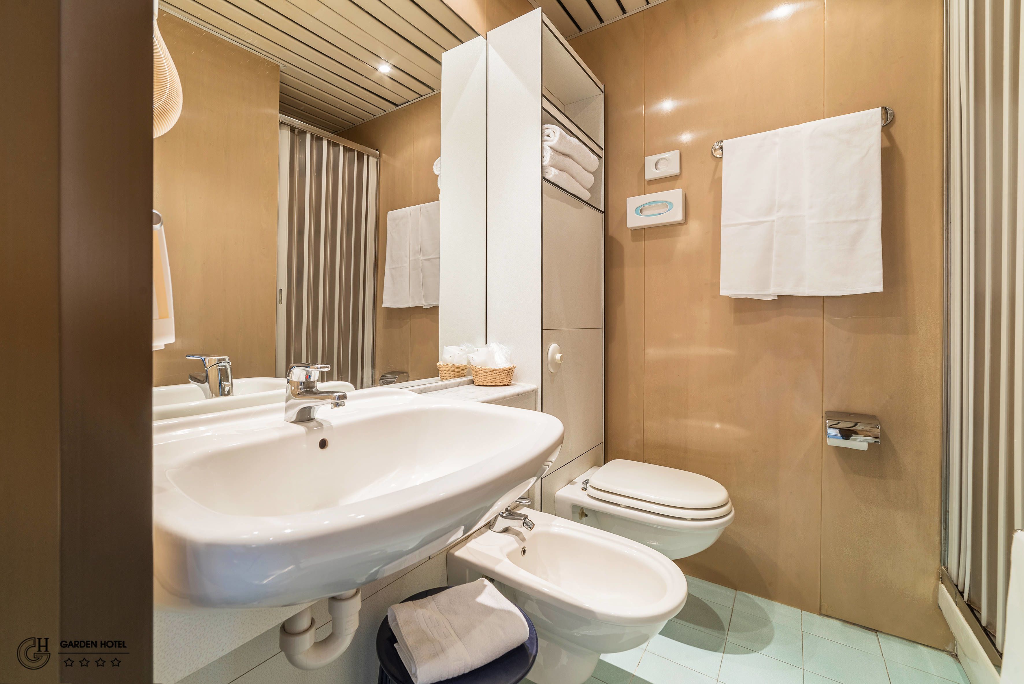 Un bagno moderno con un lavandino ampio, un bidet e un water. Asciugamani appesi al muro e un cesto di articoli da toilette.