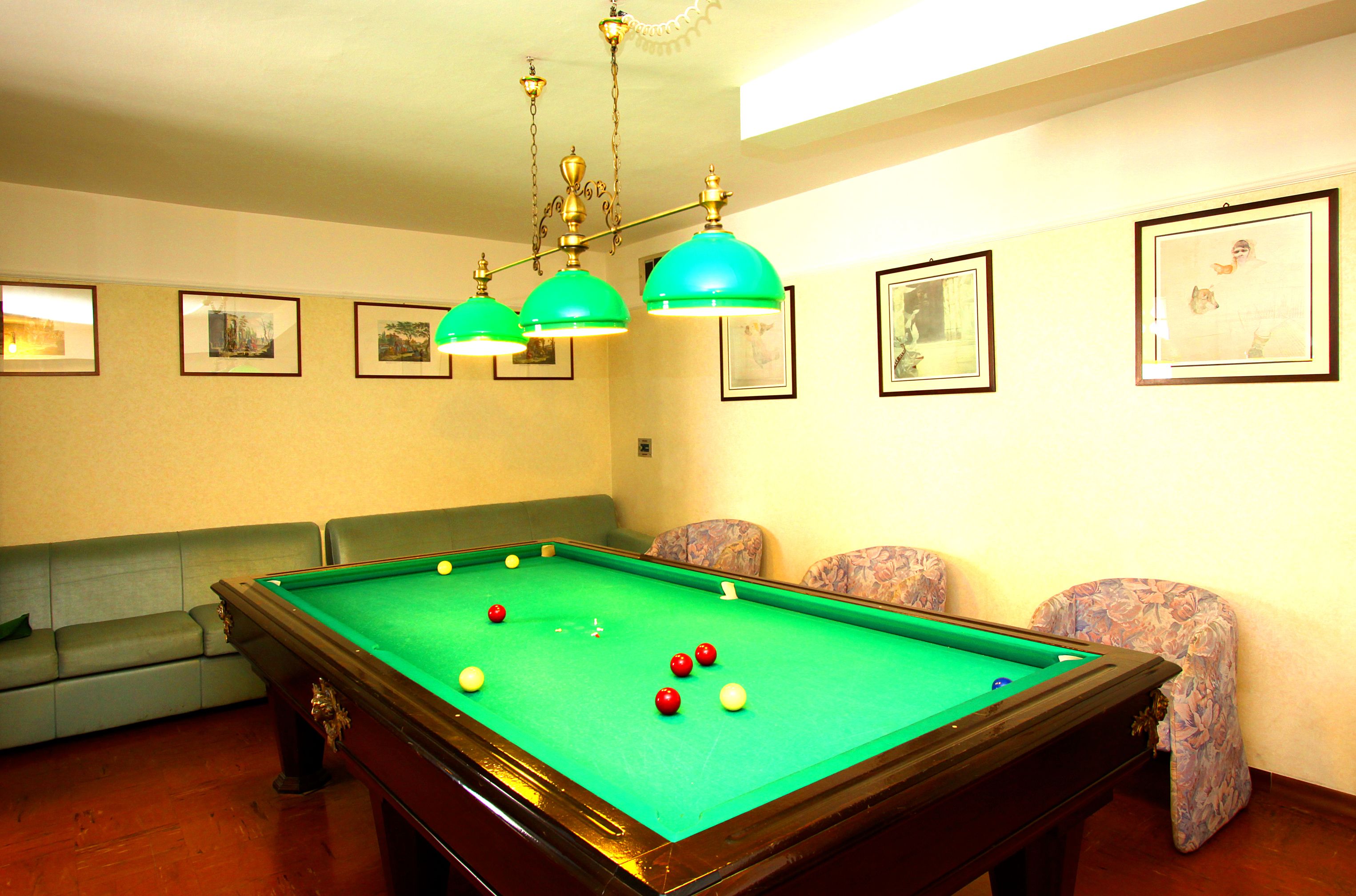 A pool table with balls, a sofa, and chairs in a room with framed pictures on the wall.