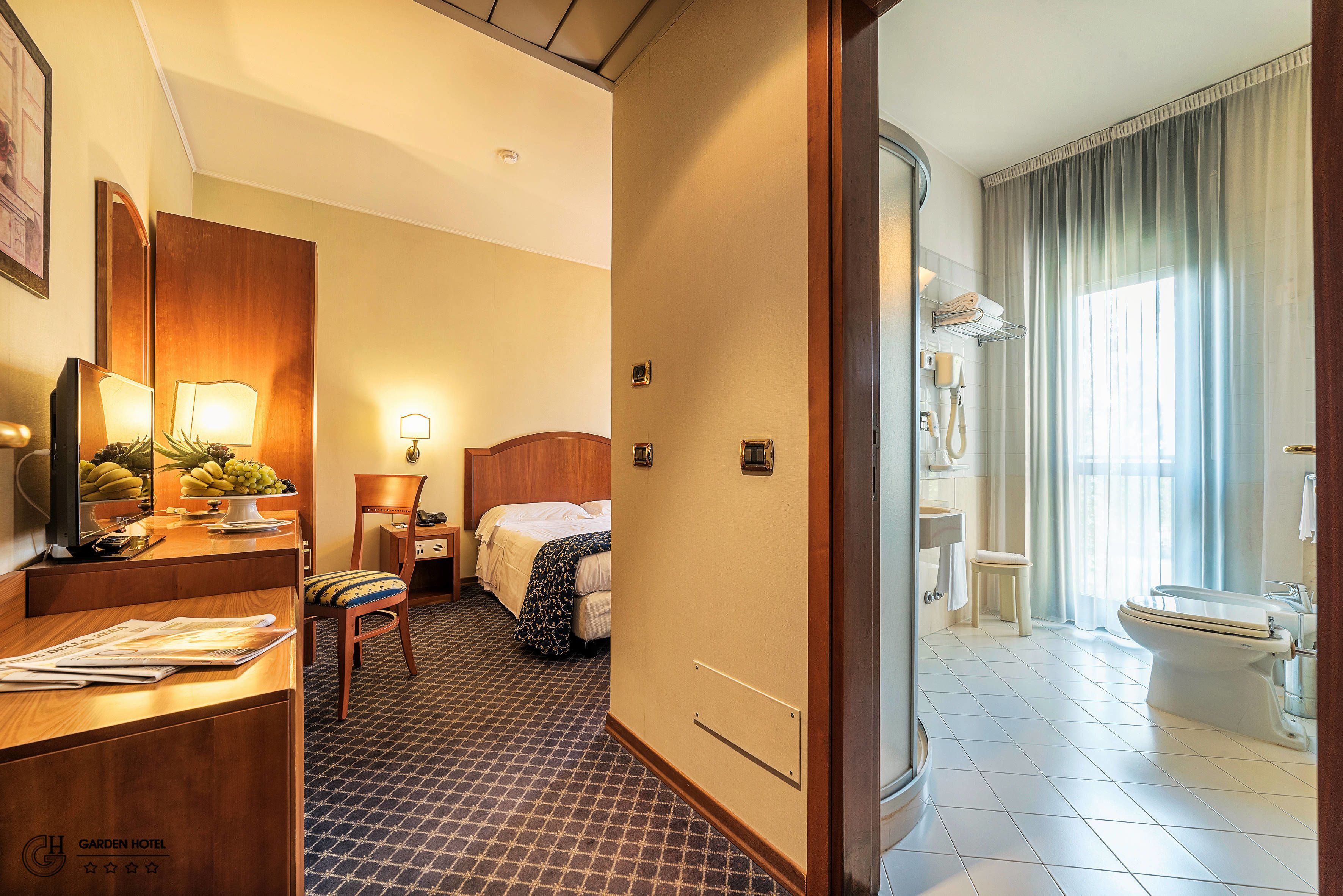 A hotel room with a bed, bedside table, lamp, and a bathroom with a toilet and sink.