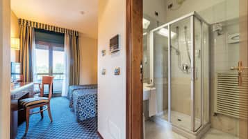 Une chambre d’hôtel équipée d’un bureau, d’une chaise, d’un lit et d’une douche séparée par des parois en verre.