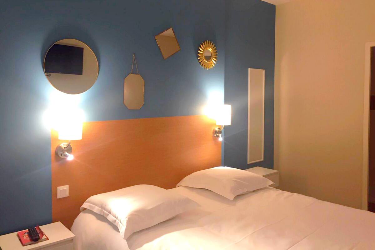 Een hotelkamer met een groot bed, twee bedlampjes, een ronde spiegel en een wandklok.