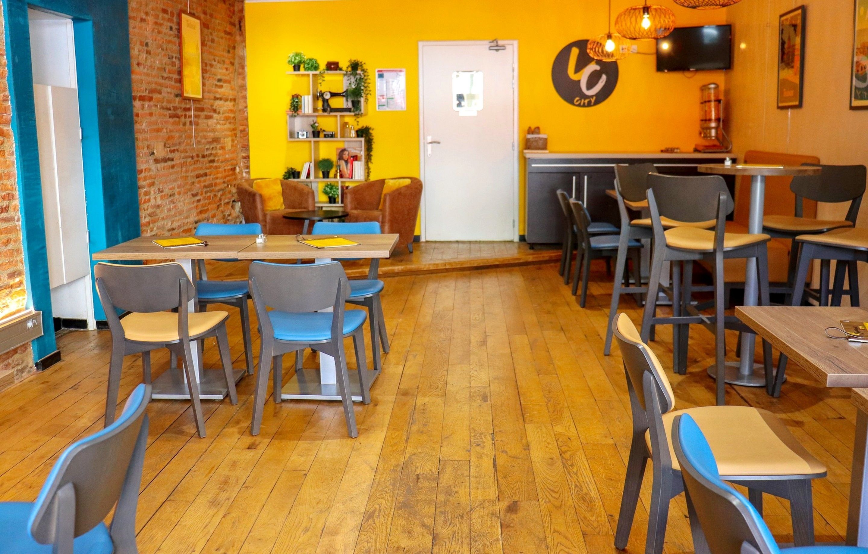 Un restaurante con suelo de madera, sillas azules y grises, una pared de ladrillo y una pared de acento amarilla con un logotipo.