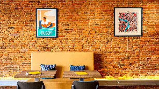 A brick wall with two framed pictures, a wooden bench, and a table with chairs. - Hotel Le Clocher de Rodez (Toulouse)
