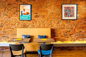 Un mur de briques orné de deux tableaux encadrés, un banc en bois et une table avec des chaises.