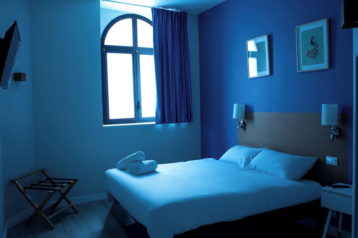 Een hotelkamer met een groot bed, een raam met gordijnen, twee wandlampen en een houten droogrek.
