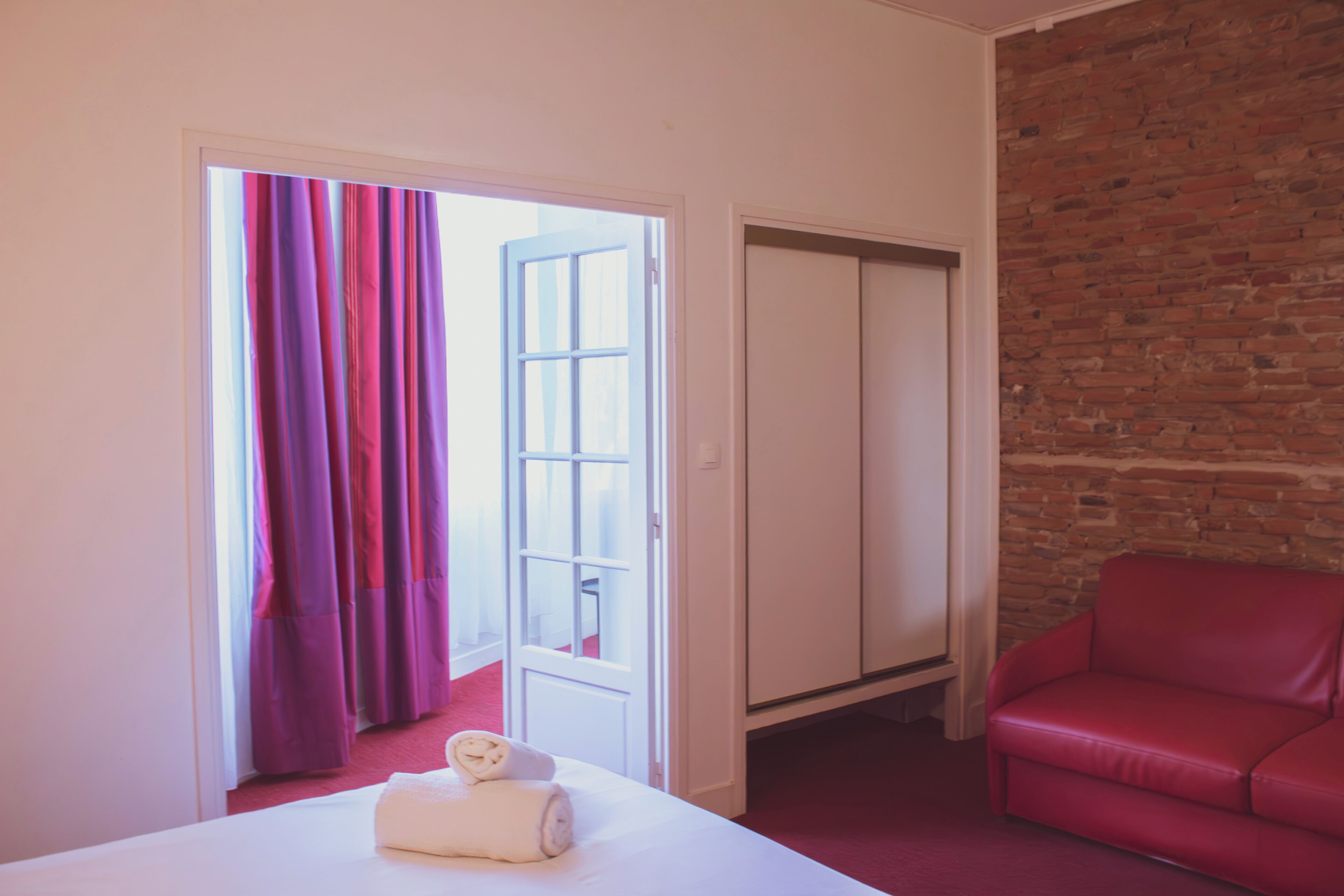 Une chambre d’hôtel avec un lit, un canapé en cuir rouge, un mur en briques et une porte donnant sur une autre pièce.