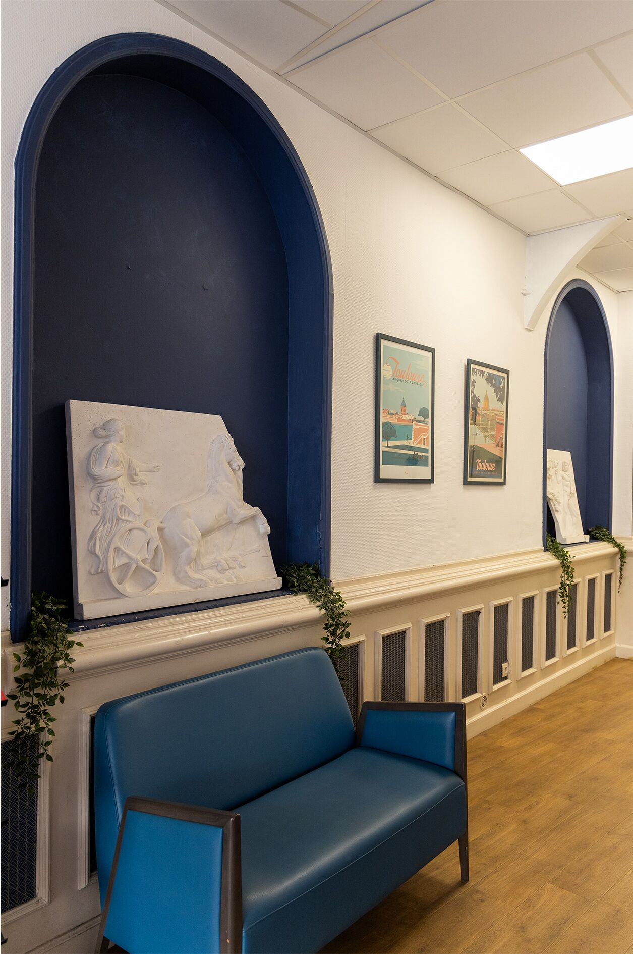 A reception area with a blue bench, a white sculpture, and two framed pictures on the wall.